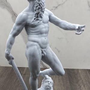 Puede incluir: Estatua gris claro de una figura masculina musculosa con barba y cabello rizado, sosteniendo un bast&oacute;n. La estatua est&aacute; de pie sobre una base con una cara esculpida. La figura est&aacute; desnuda y se&ntilde;ala con la mano derecha.