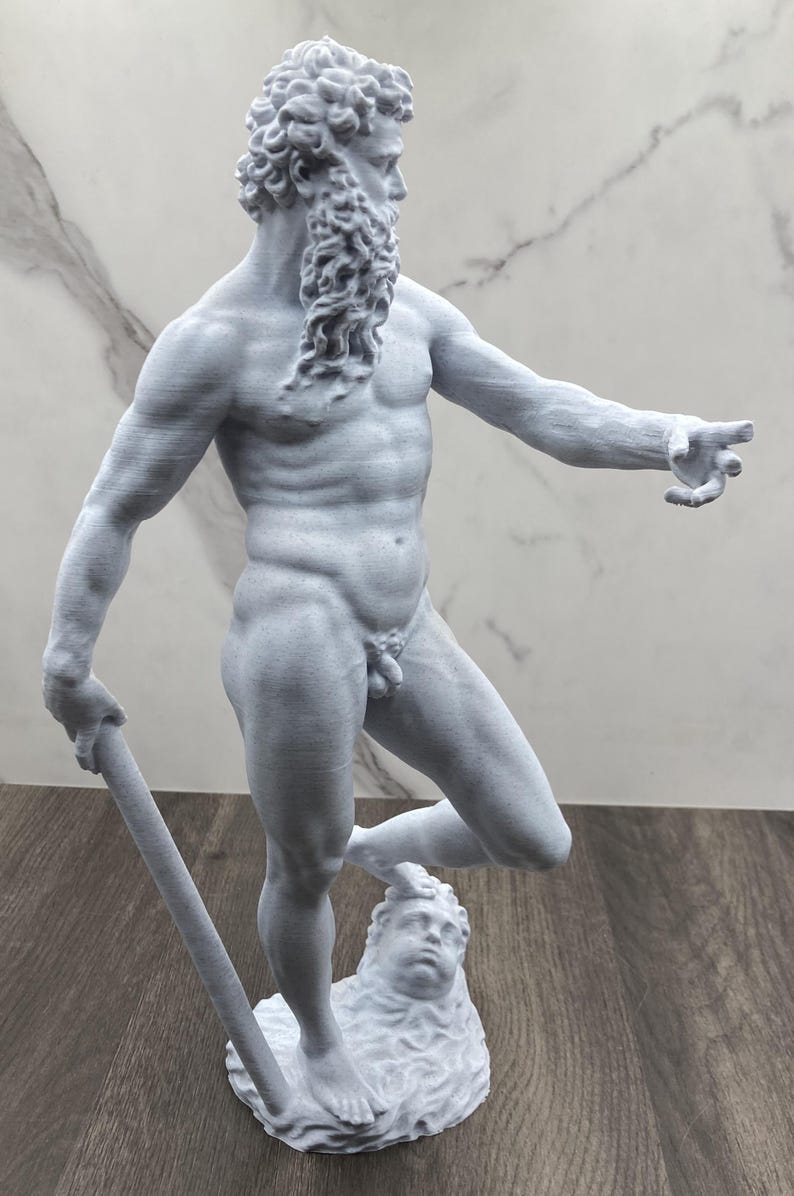 Puede incluir: Estatua gris claro de una figura masculina musculosa con barba y cabello rizado, sosteniendo un bast&oacute;n. La estatua est&aacute; de pie sobre una base con una cara esculpida. La figura est&aacute; desnuda y se&ntilde;ala con la mano derecha.