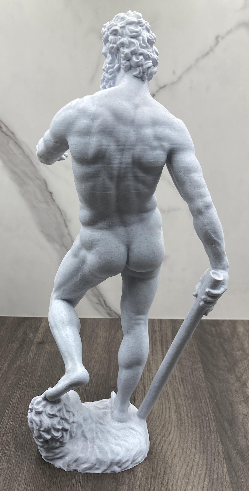 Puede incluir: Estatua gris de una figura musculosa, vista desde atr&aacute;s, sosteniendo un garrote y de pie sobre un le&oacute;n. La estatua tiene musculatura detallada y cabello rizado. La figura mide unos 30 cm de altura.