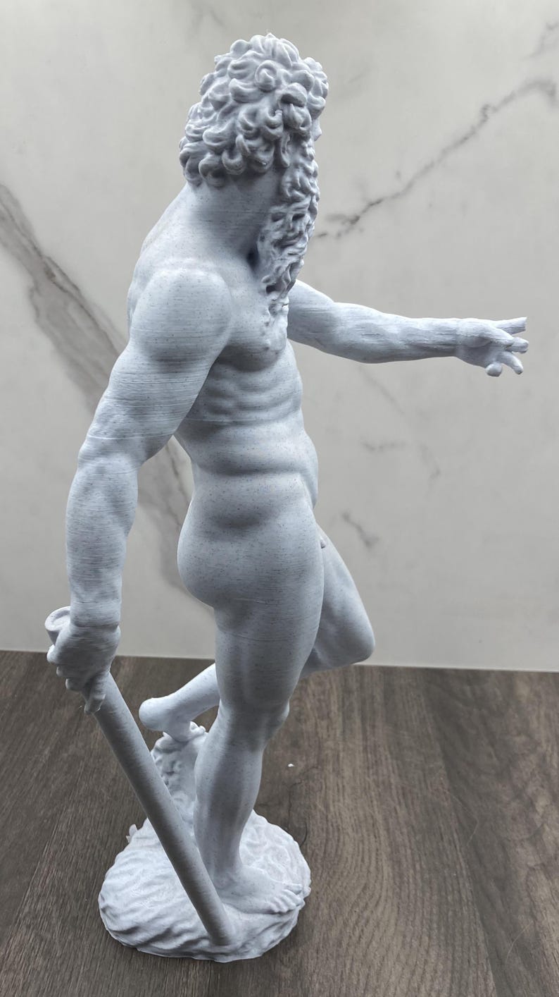Puede incluir: Estatua gris claro de una figura masculina musculosa, posiblemente un dios o h&eacute;roe cl&aacute;sico. La estatua est&aacute; desnuda, sosteniendo un bast&oacute;n y de pie sobre una base texturizada. La figura tiene cabello rizado y barba.