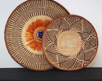May include: Two woven baskets with intricate patterns in shades of brown and beige. The larger basket has a bright orange and blue center design.