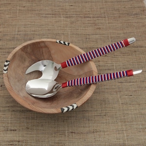 Puede incluir: Un bol de ensalada de madera con un borde blanco y negro, y un juego de dos cucharas para ensalada con mangos rayados en rojo, blanco y azul.