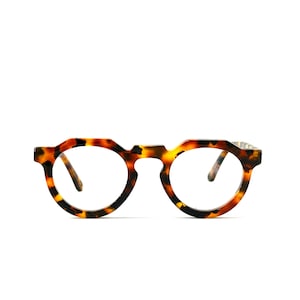 Può includere: Occhiali da vista in tartaruga con lenti rotonde e montatura marrone.