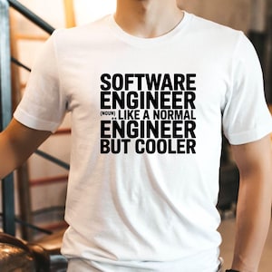 May include: White t-shirt with the text "SOFTWARE ENGINEER (noun) LIKE A NORMAL ENGINEER BUT COOLER" in black. The shirt is being worn by a person. A motorcycle is partially visible in the background.