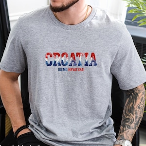 K&ouml;nnte beinhalten: Graues T-Shirt mit dem Wort "CROATIA" in Rot, Wei&szlig; und Blau, darunter der Text "IDEMO HRVATSKA!". Das T-Shirt hat einen Rundhalsausschnitt.
