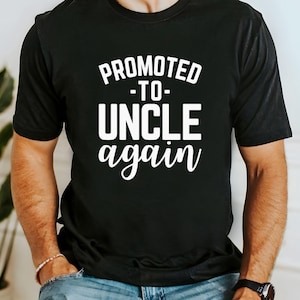 May include: Black t-shirt with the white text "PROMOTED -TO- UNCLE again". The shirt is a crew neck style and is being worn by a person. The text is in a bold, sans-serif font.