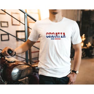K&ouml;nnte beinhalten: Wei&szlig;es T-Shirt mit dem Wort "CROATIA" in Rot, Wei&szlig; und Blau, das die kroatische Flagge darstellt. Darunter steht der Text "IDEMO HRVATSKA!". Das T-Shirt hat kurze &Auml;rmel.