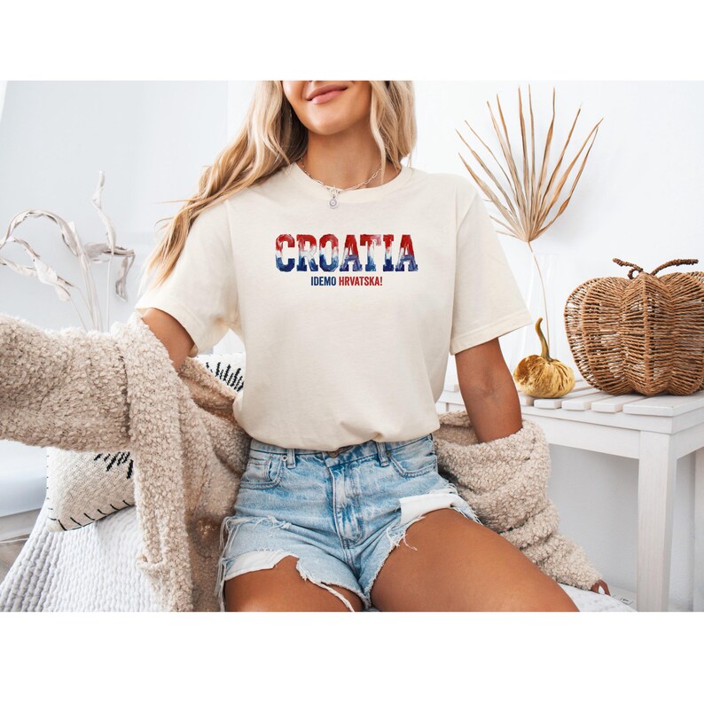 K&ouml;nnte beinhalten: Cremefarbenes T-Shirt mit dem Wort "CROATIA" in Rot, Wei&szlig; und Blau, darunter "IDEMO HRVATSKA!". Das Shirt wird mit Jeansshorts getragen. Das Gesamtthema ist Reisen und Nationalstolz.