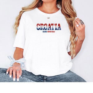 K&ouml;nnte beinhalten: Wei&szlig;es T-Shirt mit dem Wort "CROATIA" in Rot, Wei&szlig; und Blau und dem Text "IDEMO HRVATSKA!". Ein l&auml;ssiges T-Shirt f&uuml;r den Alltag.