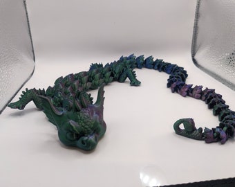 May include: A 3D printed iridescent green and purple dragon figurine with a curled tail. The dragon has a detailed head with sharp teeth and a textured body.