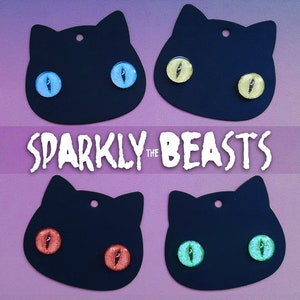 May include: Four black cat-shaped earrings with different colored glitter eyes. The eyes are blue, yellow, red, and green. The earrings are labeled "Sparkly the Beasts".
