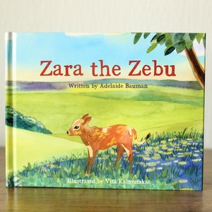 Puede incluir: Una portada de libro con una ilustración de acuarela de un ternero cebú marrón y blanco de pie en un campo de flores azules. El título del libro es "Zara the Zebu" y la autora es Adelaide Bauman. El ilustrador es Vita Kalmutska.