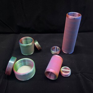 Op de afbeelding: Vijf regenboogkleurige metalen containers met deksels. De containers zijn cilindrisch en hebben een getextureerd oppervlak. De deksels zijn ook getextureerd en hebben een lichte rand.