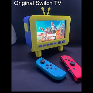 May include: A yellow and blue retro TV-shaped console with a screen displaying a video game. Two blue and red Nintendo Switch controllers are on a black surface.