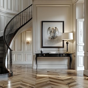 May include: An elegant entryway with a curved staircase and a black console table. A framed artwork of an angel hangs above the table, next to a lamp with a white shade. The floor has a patterned wood design.