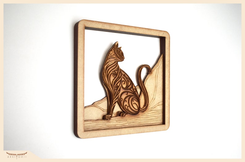 Puede incluir: Una pieza de arte de pared de madera con un dise&ntilde;o detallado e intrincado de un gato sentado en una roca. El gato est&aacute; tallado con patrones en espiral y la roca es texturizada. La pieza est&aacute; enmarcada en un simple marco de madera.