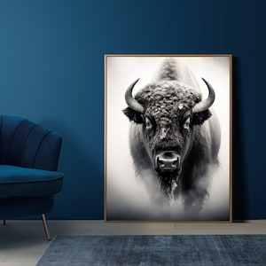 May include: Black and white photograph of a bison with a snowy background. The bison is looking directly at the camera with a serious expression. The image is framed in a wooden frame.