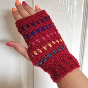May include: A red crocheted fingerless glove with a colorful geometric pattern. The pattern includes blue, pink, and yellow accents. The glove is made of a thick yarn and appears to be handmade.