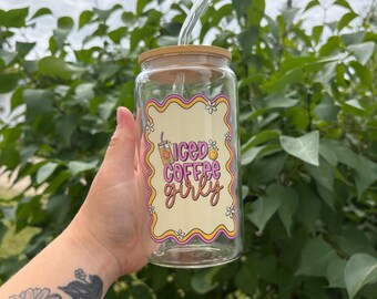 May include: A clear glass iced coffee cup with a bamboo lid and a glass straw. The cup features a colorful design with the words "iced coffee girly" in a retro font, with a floral and coffee cup graphic.