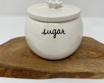 Ceramic Rae Dunn sugar bowl. New and never used. “sugar” in black cursive. 3.5 inches high and holds 8 ounces. Lid has a petite flower.