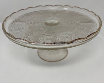 Jeanette Glass Gold Trimmed Harp Cake Stand. Vintage 1950s pedestal cake stand with scalloped edges. Preowned without cracks or chips.