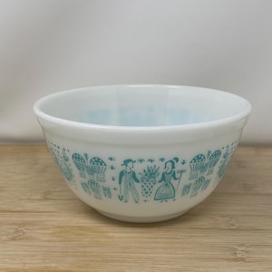 May include: White mixing bowl with a turquoise illustration of people and baskets. The bowl has a rounded shape and is made of a durable material. The turquoise design wraps around the bowl's exterior, adding a vintage touch.