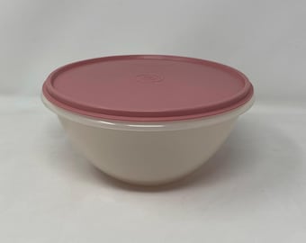 May include: A round, off-white plastic mixing bowl featuring a smooth, matte finish and a wide, flat rim. The bowl is topped with a circular, dusty rose-colored plastic lid that fits securely over the opening, creating a clean and simple storage container.
