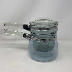 May include: A vintage glass teapot with a blue tint, featuring a clear glass lid and a stainless steel band. The teapot has two white-handled side handles. The design is a classic, retro style.