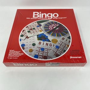 May include: A red Bingo game box with the word "Bingo" in white. The box includes a spinner card, Bingo cards, plastic markers, and instructions. The game is designed for ages 7 and up.