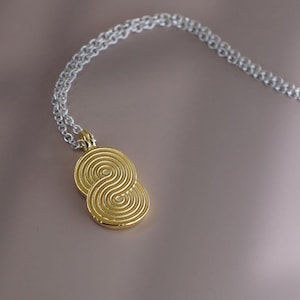 Pode incluir: Um colar de ouro com um pingente com um design de dupla espiral. O colar é feito de uma corrente de prata.
