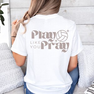 May include: White t-shirt with a brown graphic that says "Play Like You Pray" with a volleyball graphic.