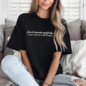 May include: Black t-shirt with white text that reads "Jesus, I surrender myself to you. Take care of everything."