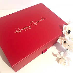 May include: A red gift box with a gold inscription that reads "Happy Diwali".