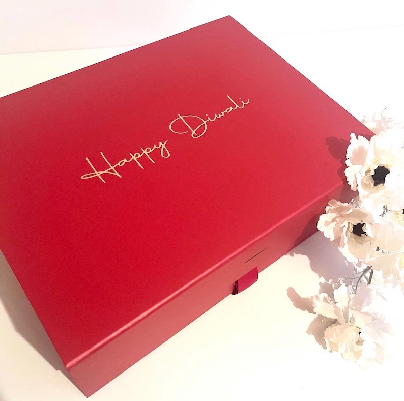 May include: A red gift box with a gold inscription that reads "Happy Diwali".