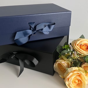 May include: Two gift boxes, one navy blue and one black, both tied with matching ribbon bows. The boxes are stacked on top of each other. A bouquet of yellow roses is in the foreground.