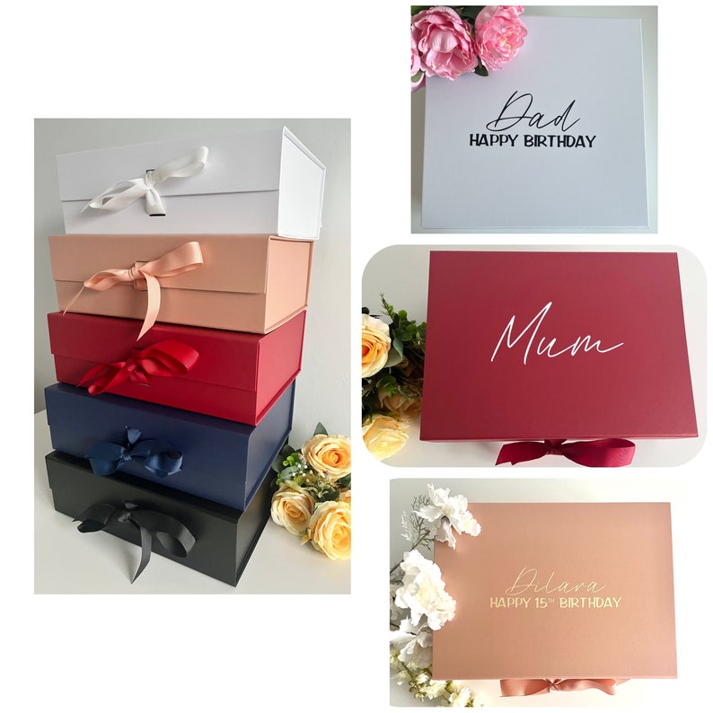 May include: Four stacked gift boxes with different colored lids and ribbons. The top box is white with a black inscription that reads "Dad Happy Birthday". The second box is pink with a black inscription that reads "Mum". The third box is red with a gold inscription that reads "Dilara Happy 15th Birthday". The bottom box is black.