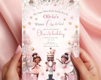 May include: A pink and gold invitation for a first birthday party with a winter wonderland theme. The invitation features a Nutcracker, two ballerinas, and a winter scene with snowflakes and trees. The text on the invitation reads "The Sugar Plum Fairy Invites You To Olivia's Winter Onederland Join Us To Celebrate Olivia's 1st Birthday Saturday, November 15th 1 pm Olivia's home 123 your street, your city RSVP Sarah 123-456-7500"