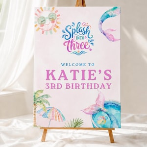 May include: A birthday sign on a wooden easel, featuring a watercolour design. The sign says "Splash into Three" and "Welcome to Katie's 3rd Birthday." The design includes a sun, mermaid tail, palm tree, and umbrella.
