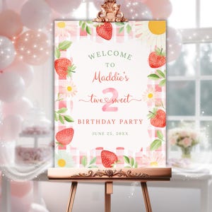 May include: A welcome sign for a birthday party, featuring a pink and white gingham background. The sign includes the text "Welcome to Maddie's two sweet birthday party" with strawberry and daisy illustrations. The sign is displayed on a wooden easel.