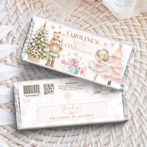 May include: A rectangular chocolate bar wrapper featuring a nutcracker, a ballerina, a Christmas tree, and a pink tree. The text reads Caroline's Winter ONEderland and Thank you for coming to my party. The back includes a barcode and ingredients.