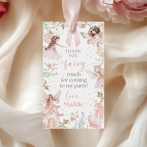 May include: A rectangular tag with a pink ribbon, featuring watercolor illustrations of fairies and floral elements. The tag reads "Thank You Fairy, much for coming to my party! love, Maddie."