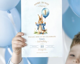 Puede incluir: Una invitación azul y blanca con una ilustración de acuarela de un conejito sosteniendo un globo azul con el número uno. El texto dice "Some Bunny is turning 1" y "Liam's first birthday". La invitación incluye la fecha, la hora y la ubicación de la fiesta.