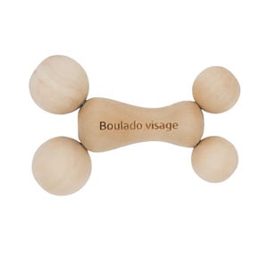 Può includere: Uno strumento per massaggio facciale in legno chiaro. Lo strumento ha una sezione centrale curva con il testo "Boulado visage" e quattro estremità arrotondate a forma di sfera. Il design è simmetrico e sembra essere realizzato in legno naturale.