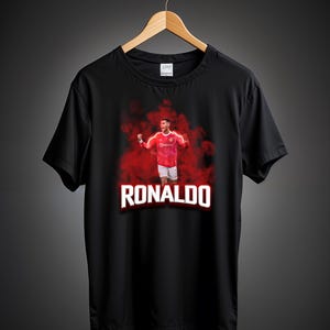 May include: Black t-shirt with a red and white image of a soccer player in a red jersey with the name "RONALDO" printed in white letters.