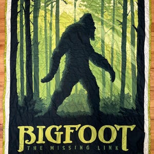 Puede incluir: Una colcha verde y negra con una silueta de Bigfoot caminando por un bosque. El texto "BIGFOOT THE MISSING LINK" est&aacute; impreso en amarillo en la parte inferior.
