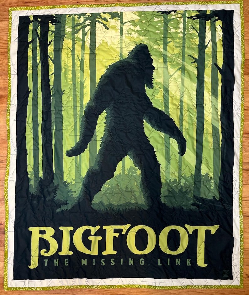 Puede incluir: Una colcha verde y negra con una silueta de Bigfoot caminando por un bosque. El texto "BIGFOOT THE MISSING LINK" est&aacute; impreso en amarillo en la parte inferior.