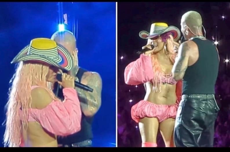 May include: A performer with long pink hair wears a pink two-piece outfit consisting of a long-sleeved crop top and puffy shorts, paired with a multi-colored cowboy hat featuring yellow, white, black, and red stripes, while holding a black microphone.