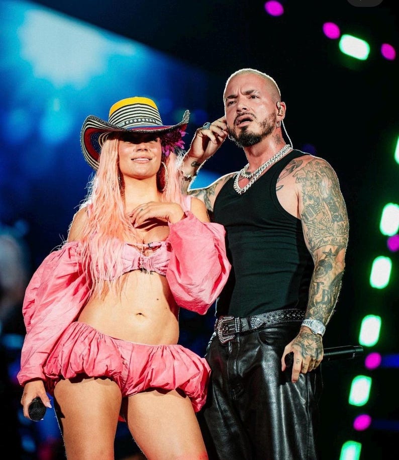 May include: A person with long pink hair wears a multi-colored striped cowboy hat and a pink two-piece outfit with puffy sleeves and a ruffled skirt. Beside them, a person with tattoos wears a black tank top, black leather pants, and a silver chain.