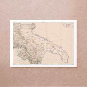 May include: A framed vintage map of Puglia, Italy, in a neutral colour palette. The map features detailed geographical information, including cities, towns, and topographical features. The map is set against a light background and framed in white.