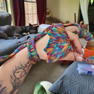 Peut inclure: Une personne est en train de crocheter un dragon color&eacute; avec une longue queue. Le dragon est fait de plusieurs couleurs, dont le rouge, l'orange, le jaune, le vert, le bleu et le violet.